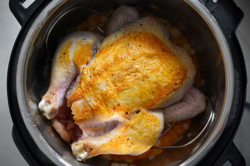 An overhead shot of a whole chicken, breast side up, on top of the steamer rack in an Instant Pot.
