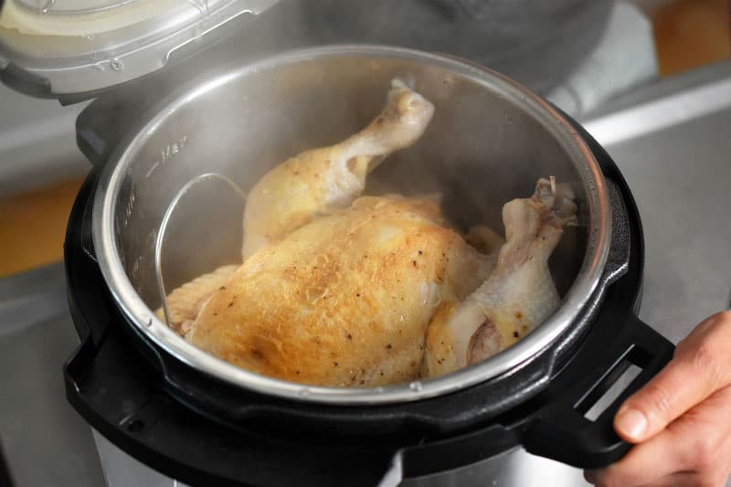 An open Instant Pot that has a steaming cooked whole chicken inside.