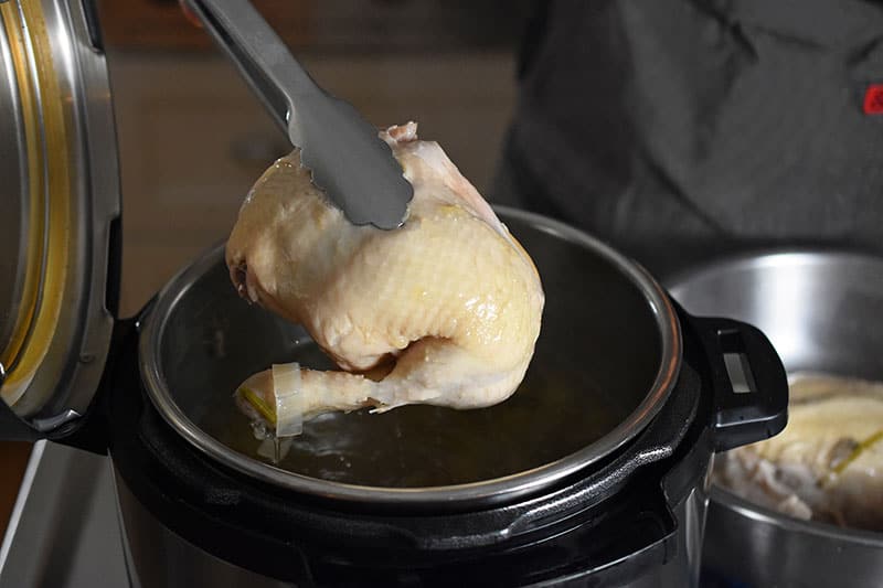 Transferring the cooked chicken from the Instant Pot to a bowl with a pair of tongs