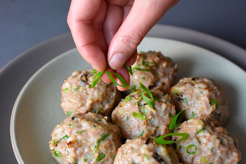 Garnishing a plate of Wonton Meatballs with sliced scallions