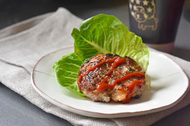 A Wonton Meatball patty on a piece of lettuce and drizzled with sriracha