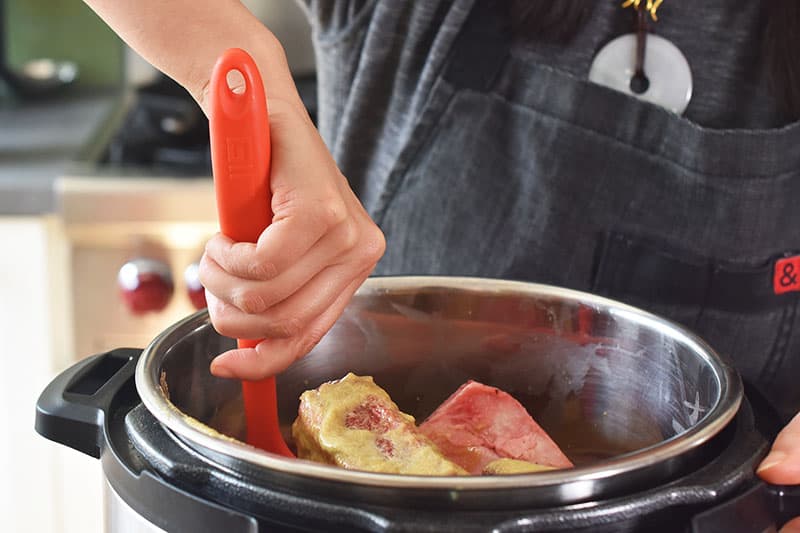 Using a spatula to mix the ingredients in the Instant Pot and to ensure liquid reaches the bottom of the pot