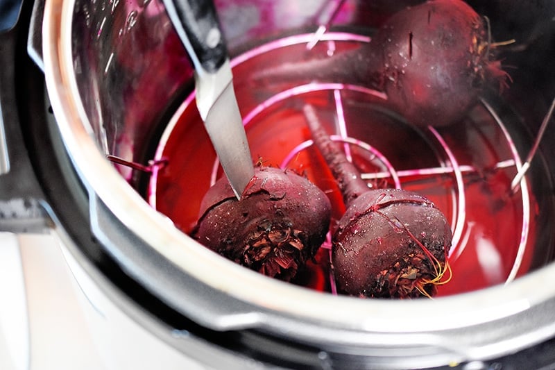 Three cooked beets are in an instant pot. Someone is stabbing one with a knife to check its doneness.
