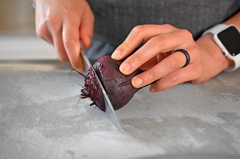 Someone slicing off the bottom root of a cooked beet.