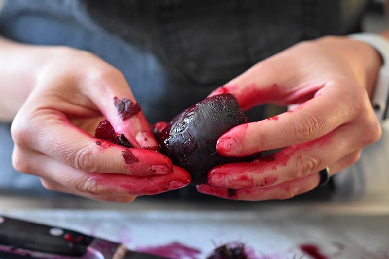 Someone peeling the skin of a cooked beet.