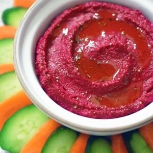 An overhead shot of paleo, Whole30, and vegan beet hummus in a white bowl surrounded by carrot and cucumber slices.