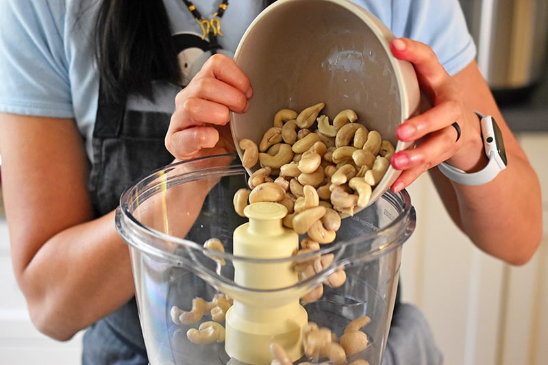 Adding the soaked cashews to a food processor.
