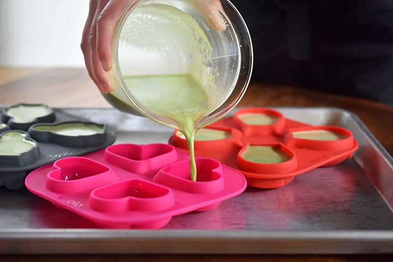 Someone pouring the liquid ingredients of the matcha coconut gummies into silicone molds.
