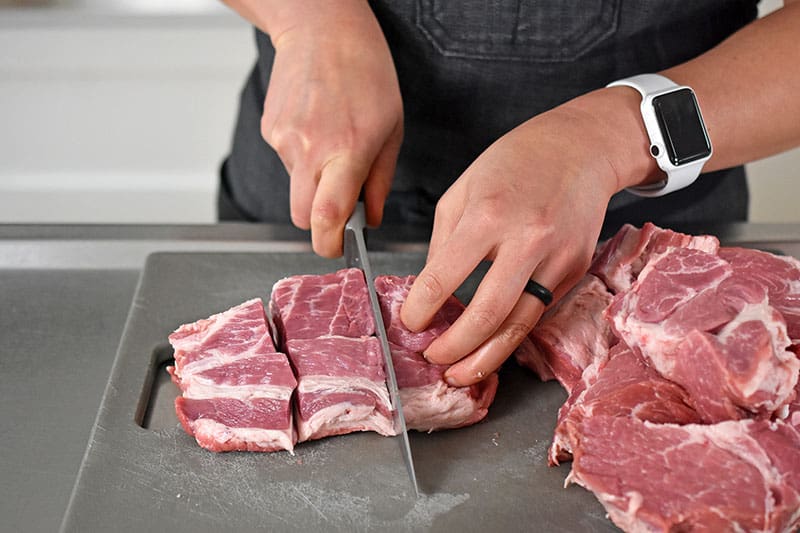 Slicing pork shoulder roast into 2-inch cubes