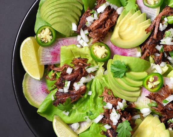 An overhead shot of Instant Pot (Pressure Cooker) Carnitas on a bed of lettuce with sliced peppers, avocado, and radishes.