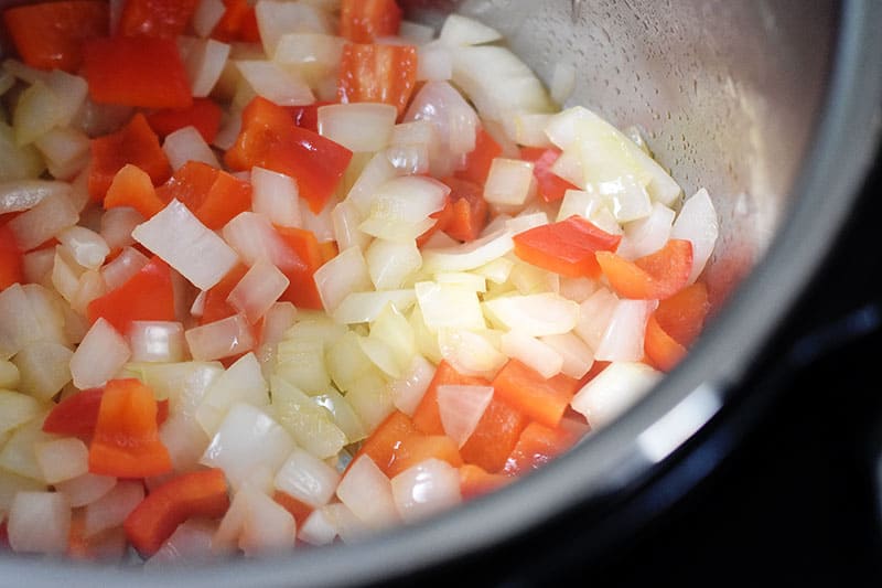 A close up of diced onions and red bell peppers being sautéed in an open Instant Pot.