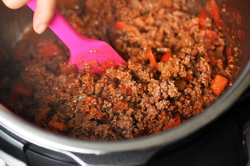 A close-up of Instant Pot Ground Beef Chili where the beef is browned and is being stirred with a bright pink silicone spatula.