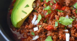 A closeup image of a bowl of Instant Pot Ground Beef Chili topped with sliced avocado, diced onions, and minced cilantro.