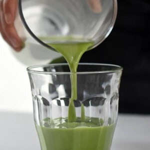 Someone pouring Cold Matcha Latte into a clear glass.