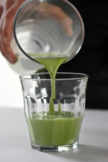 Someone pouring Cold Matcha Latte into a clear glass.