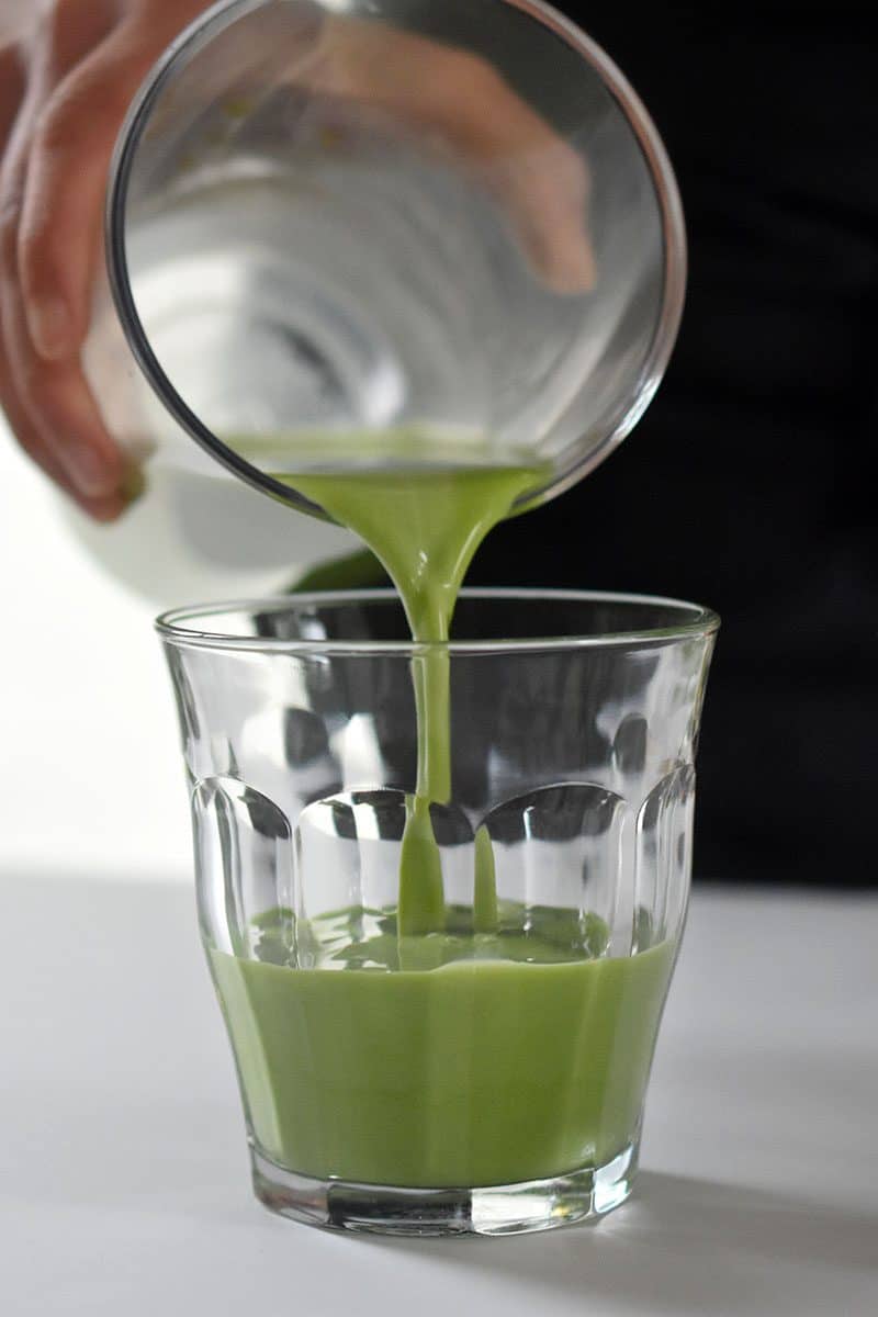 Someone pouring iced matcha latte into a clear glass.
