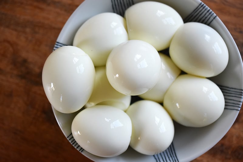 An overhead shot of hard boiled eggs in a blue and white bowl.
