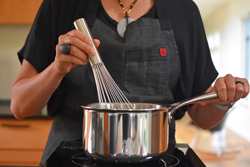 A person whisking the sweetened coconut milk in a small saucepan