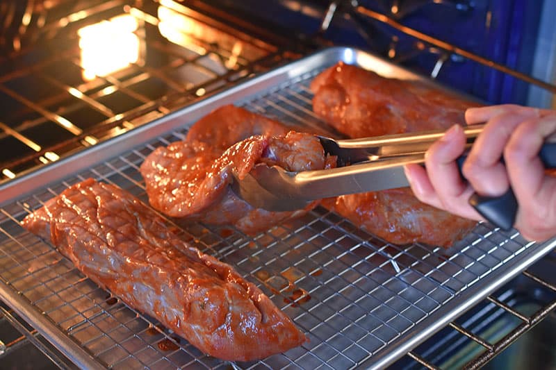 A pair of tongs are seen flipping Paleo Char Siu (Chinese BBQ Pork) as it bakes in the oven.