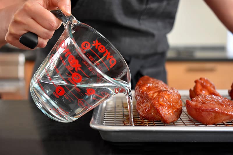 Water is poured into the rimmed baking sheet of the Paleo Char Siu (Chinese BBQ Pork) 