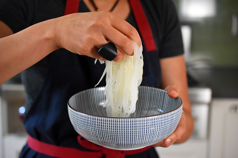 Someone placing the chilled daikon noodles into a bowl.