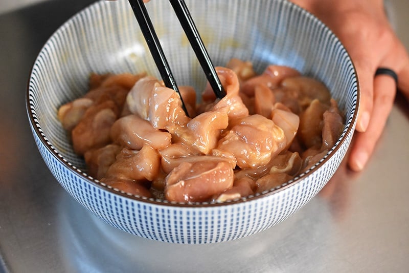 Someone mixing marinated chicken thigh pieces with a pair of chopsticks. 