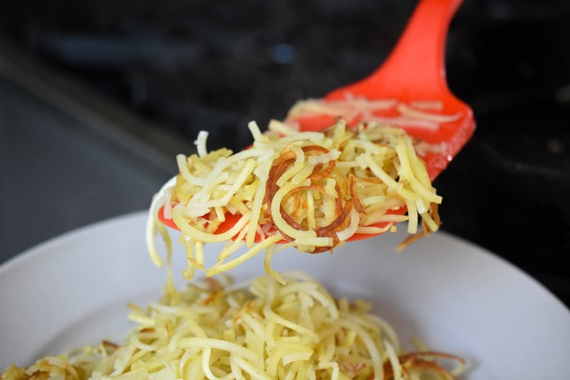 A red spatula is transferring crispy spiralized sweet potato noodles to a platter.