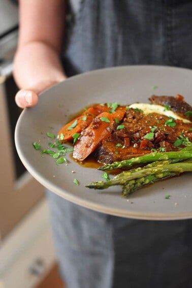 A side view of someone holding a plate with a slice of Instant Pot Yankee Pot Roast and roasted asparagus