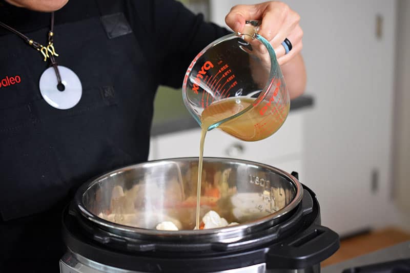 Someone pouring broth into the metal insert of an Instant Pot.