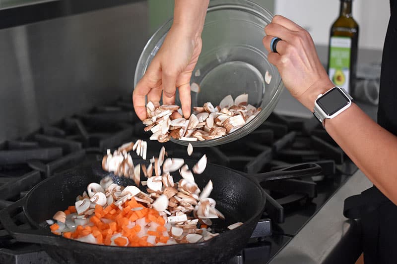Frying diced carrots, onions, and sliced mushrooms in a large cast iron skillet.