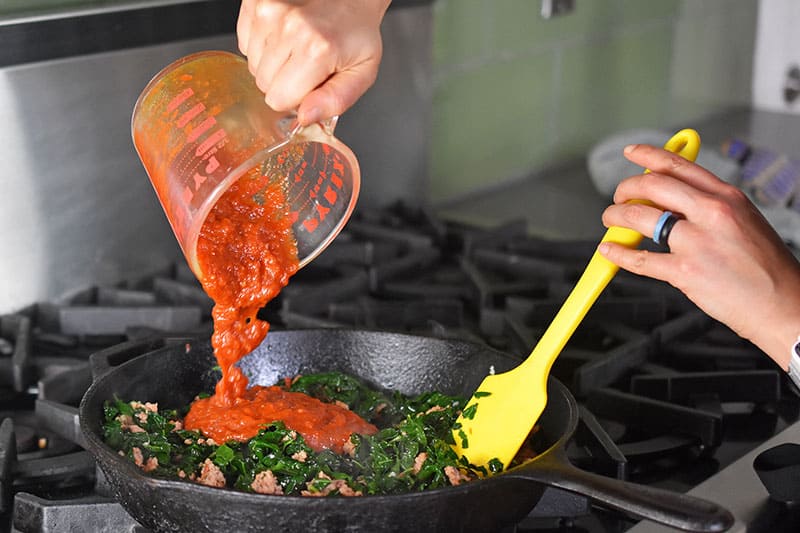 Marinara sauce is added to the italian sausage and kale in the cast iron skillet