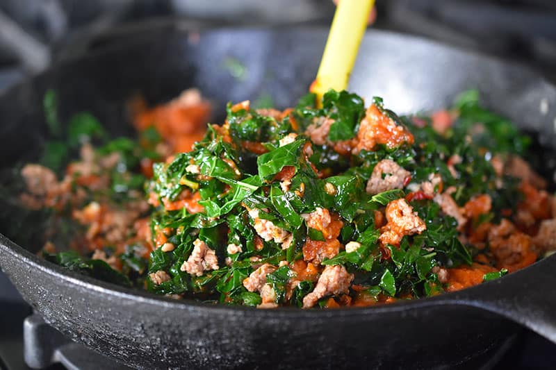 A closeup of the cooked sausage, kale, and marinara sauce in the cast iron skillet.