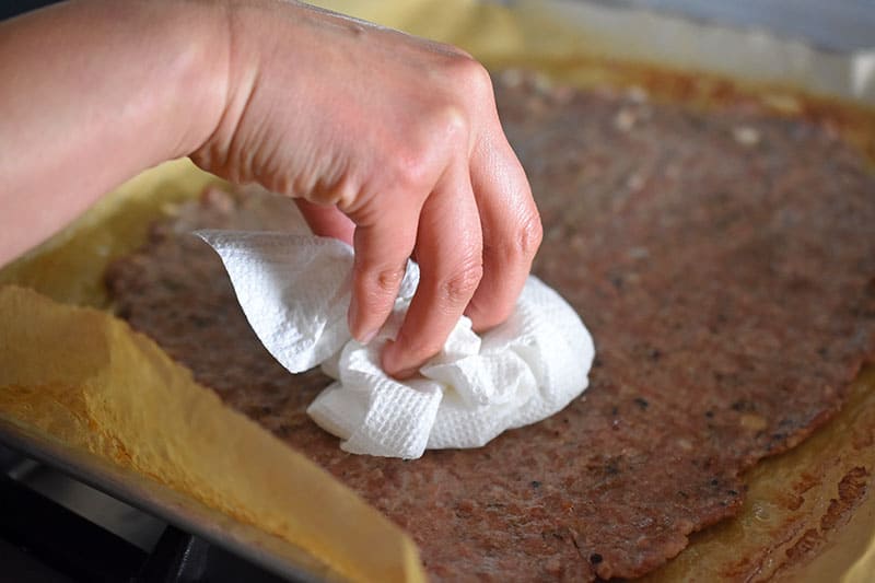 Blotting the cooked sausage crust with a paper towel to remove some of the cooking grease.