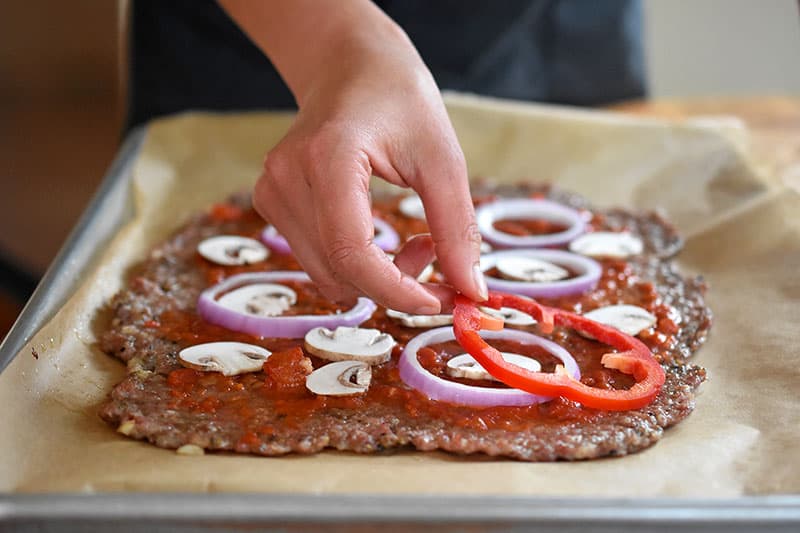 Placing toppings on a meatza.