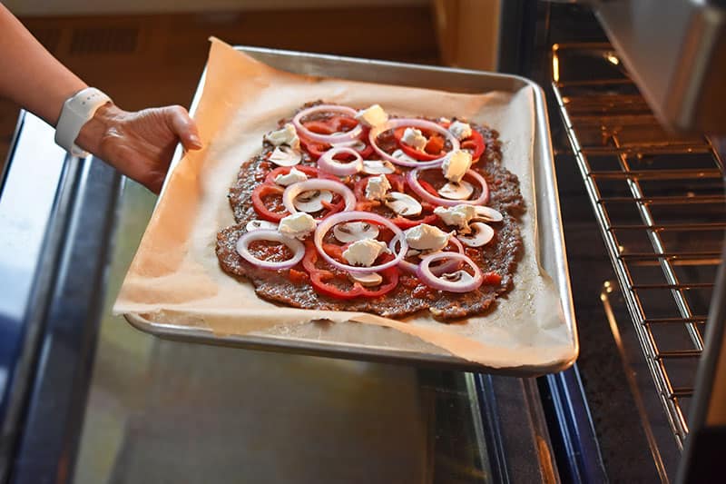 Placing a meatza into the oven to finish baking.