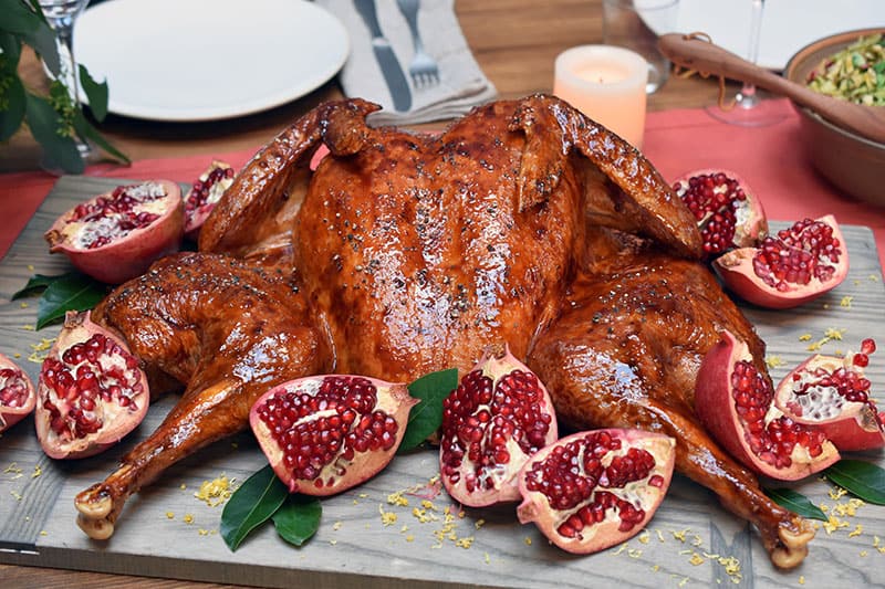 A shot of a paleo spatchcock turkey that is on a cutting board surrounded by pomegranates.