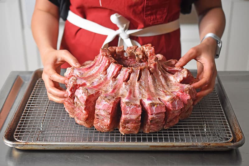 Someone placing the Magic Crown Roast of Pork on a wire rack on a sheet pan.