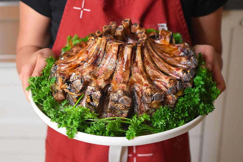 Someone holding a crown rack of pork that is ready to be carved at the Thanksgiving table
