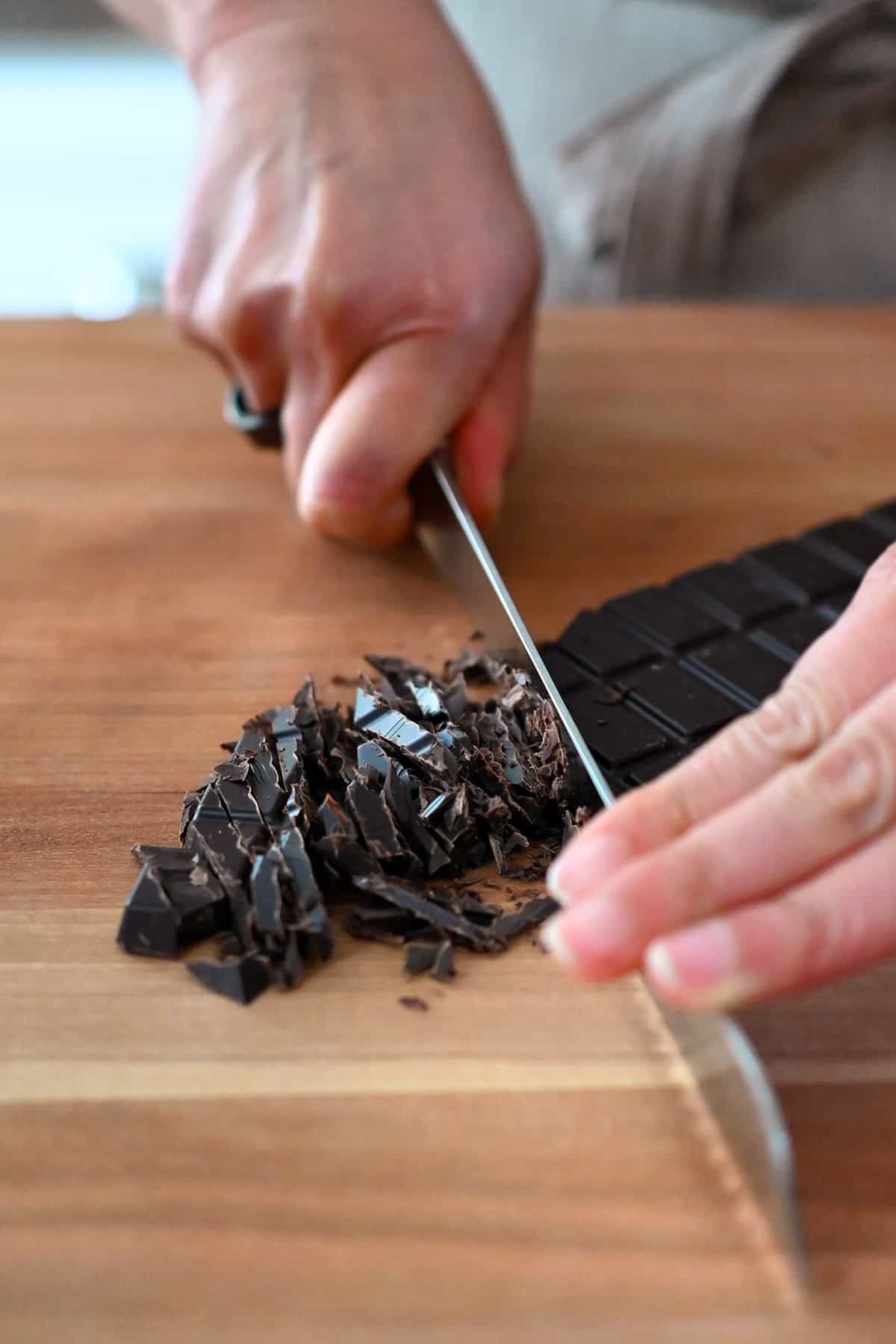 A closeup of thinly slicing a bar of dark chocolate with a chef's knife