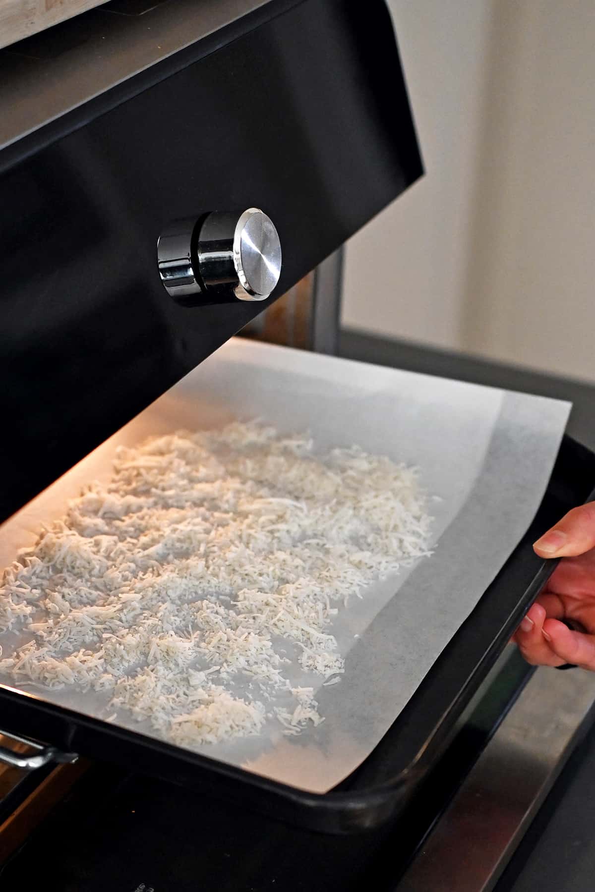 A rimmed baking sheet with a layer of shredded coconut is placed in a toaster oven.