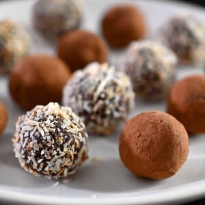 A closeup of a plate filled with Nom Nom Paleo vegan chocolate truffles topped with cocoa powder or toasted shredded coconut.