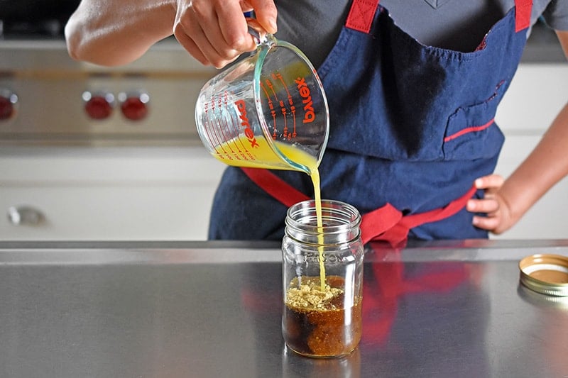 Pouring orange juice into a jar filled with All-Purpose Stir-Fry Sauce ingredients
