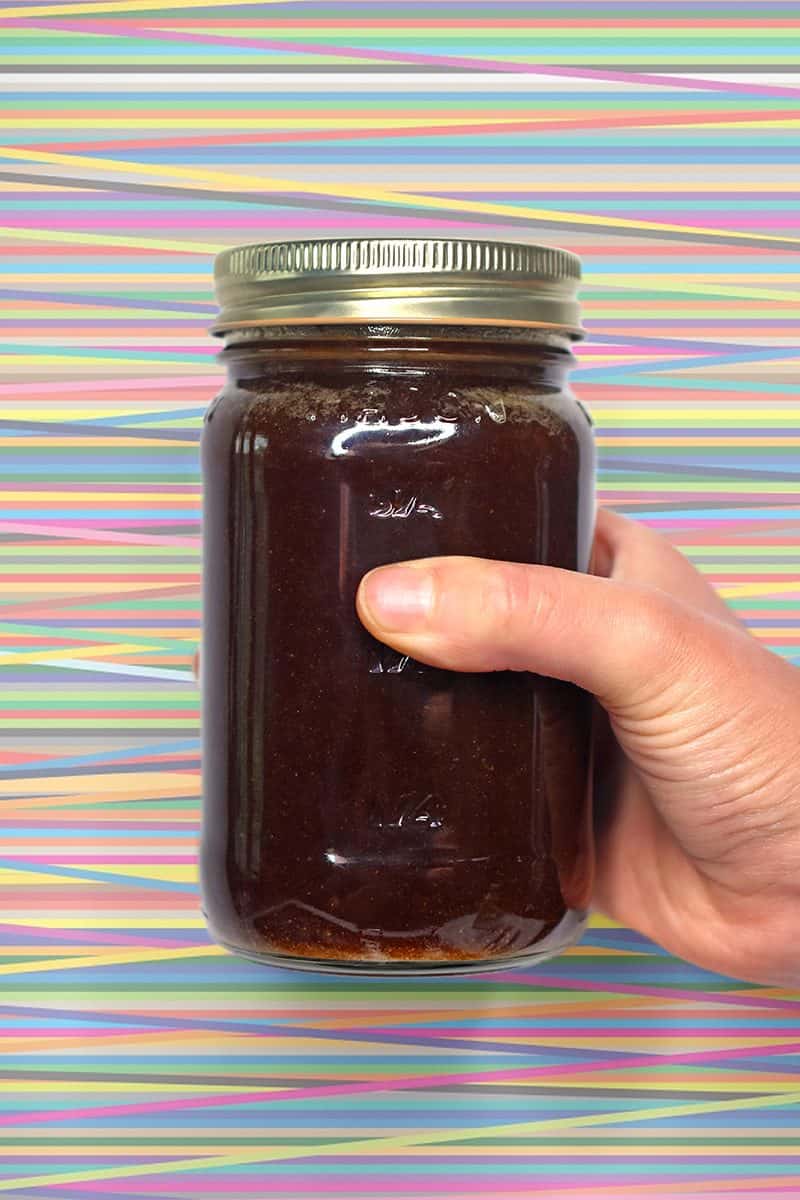 A hand holding a mason jar filled with All-Purpose Stir-Fry Sauce in front of brightly colored background.