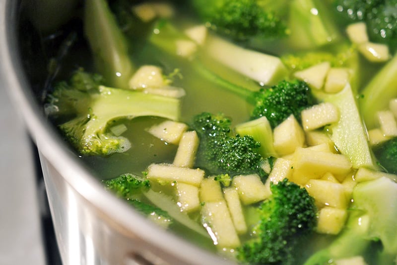 A closeup of a pot of Curried Cream of Broccoli Soup filled with broccoli florets and diced apple.
