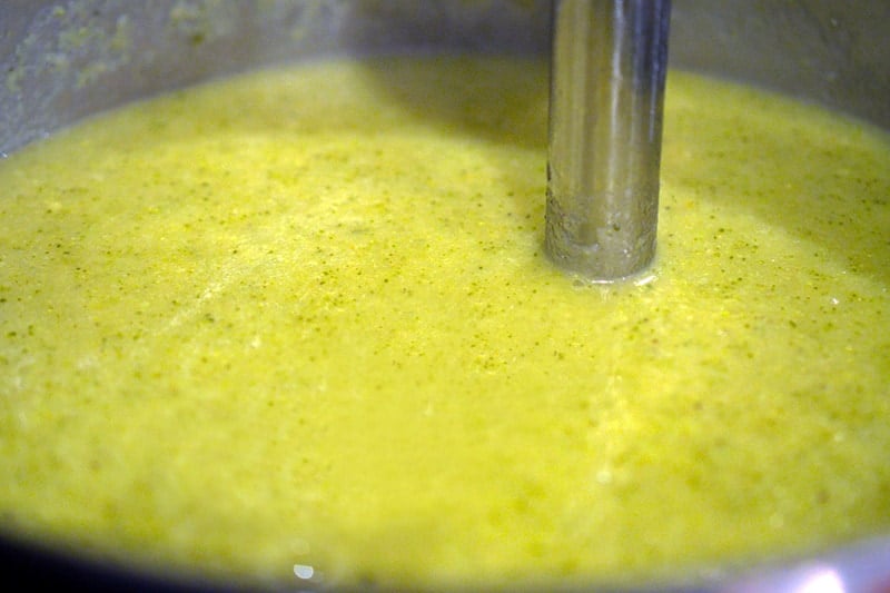 A pot with blended Curried Cream of Broccoli Soup with the immersion blender still in the soup.