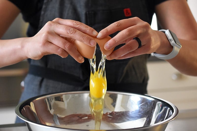 Cracking an egg into a large metal mixing bowl.