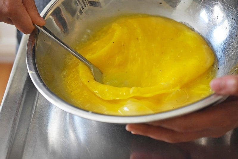 An overhead shot of someone whisking eggs in a metal bowl with a fork.