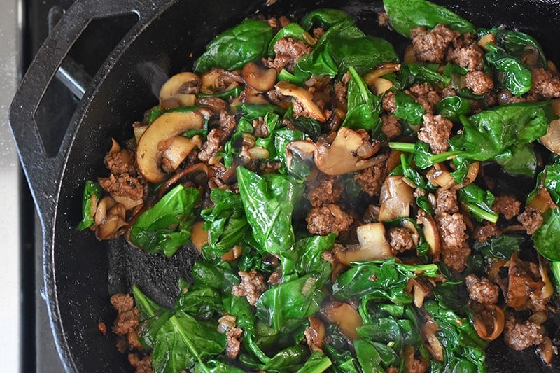 An overhead skillet with the cooked ground beef, mushrooms, and spinach.