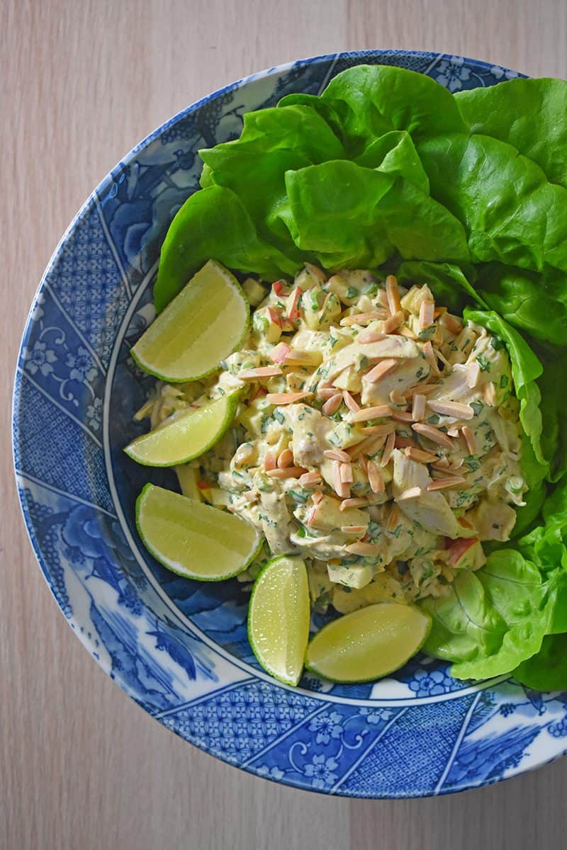 An overhead shot of a bowl of madras chicken salad with butter lettuce and limes.