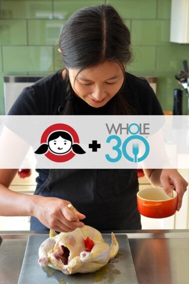 A brunette brushing ghee on a whole chicken. There is a banner that show the Nom Nom Paleo Logo + Whole30
